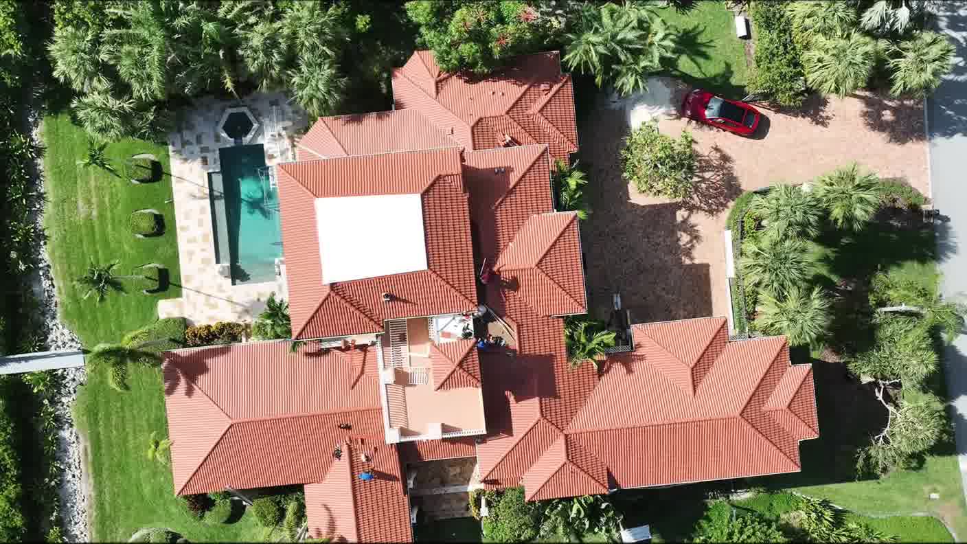 Aerial view of a tile-roofed home with a screened pool and landscaped garden