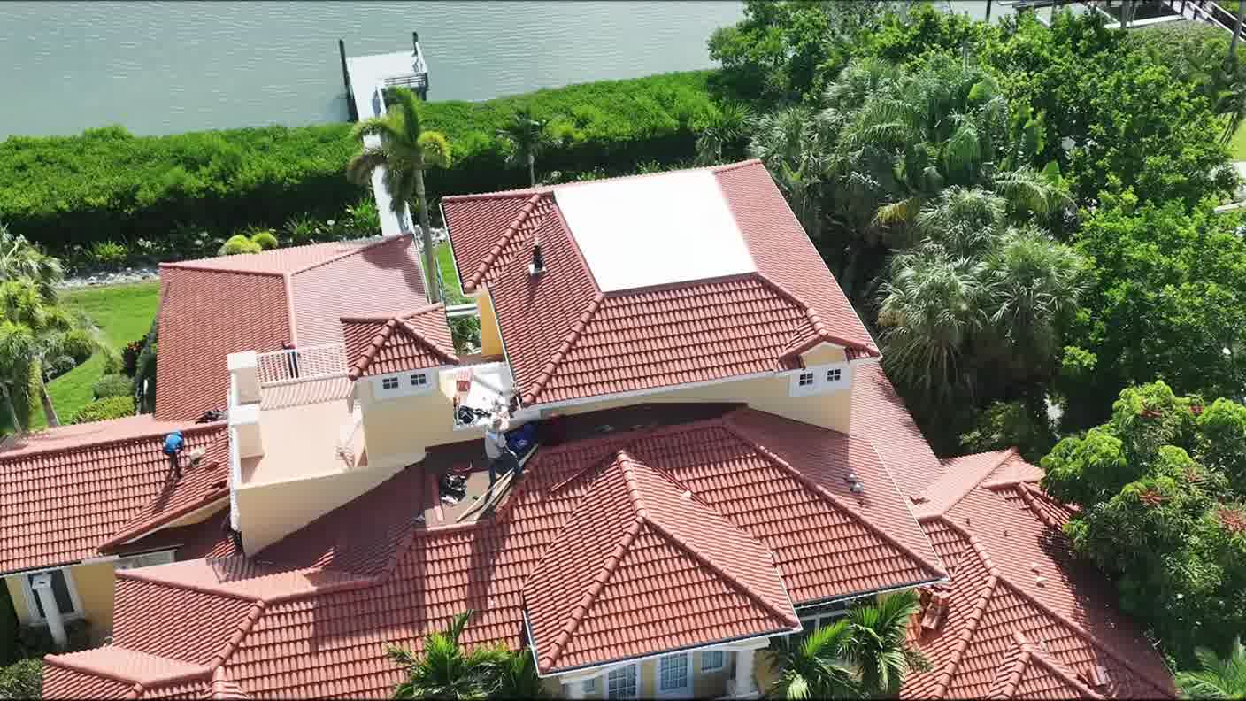 Aerial view of a tile-roofed home with a seawall and dock behind it