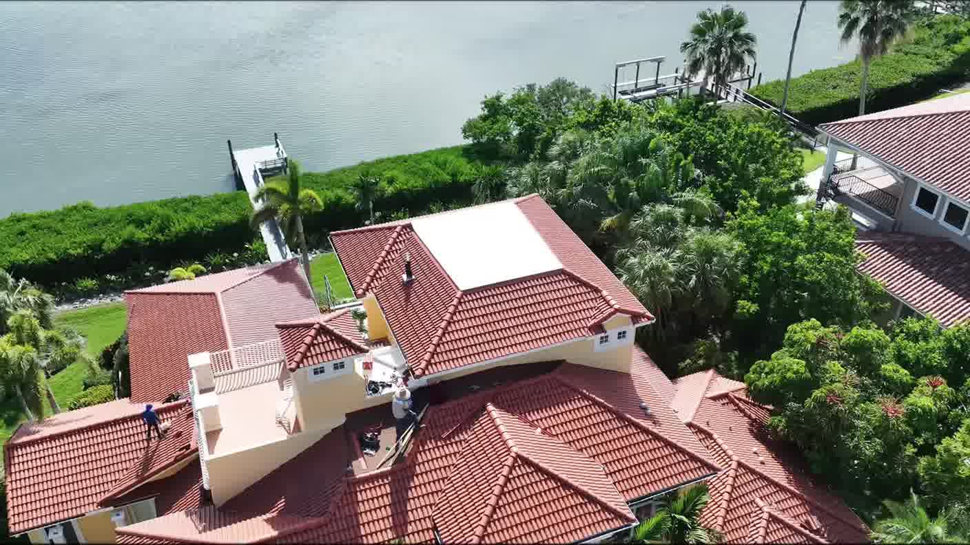 Aerial view of a tile-roofed waterfront home surrounded by palms