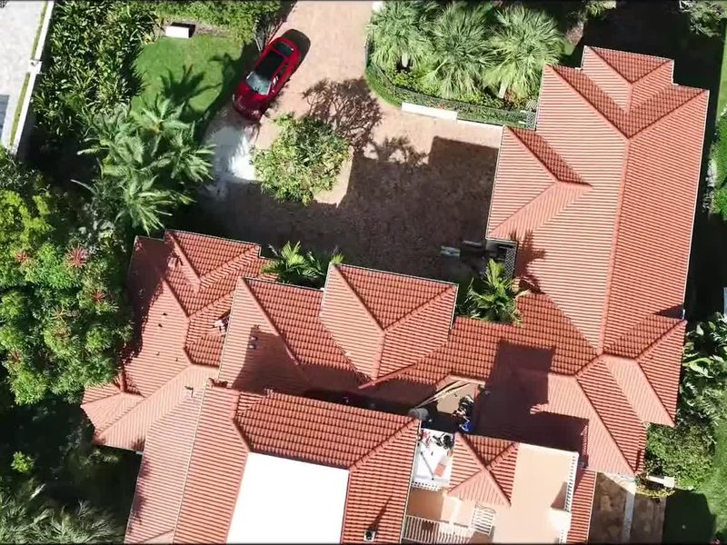 Aerial view of a finished barrel tile roof on a large home surrounded by palms